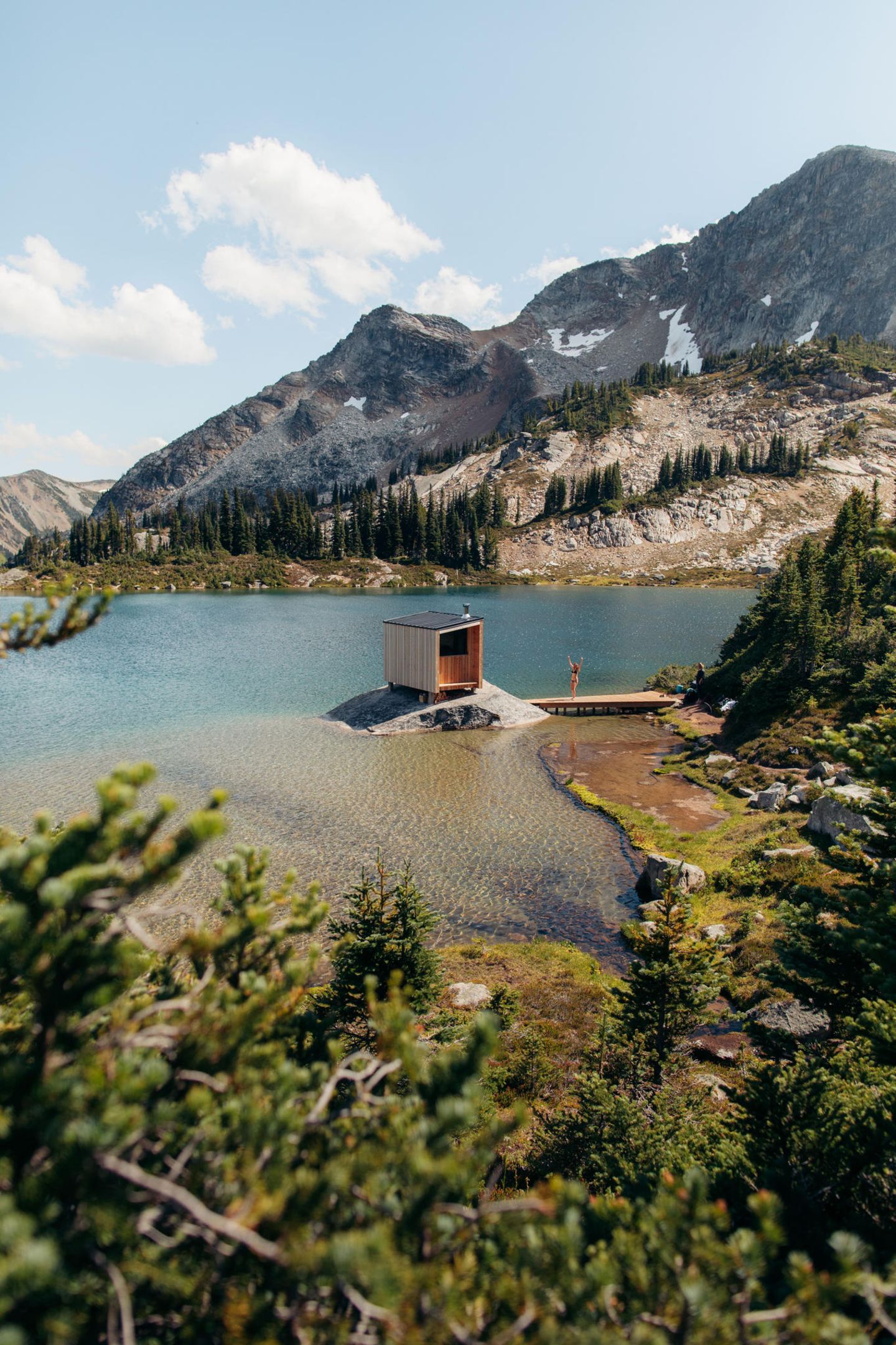 See mit kleinem Felsen, darauf eine modern designte Sauna