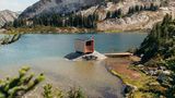 See mit kleinem Felsen, darauf eine modern designte Sauna