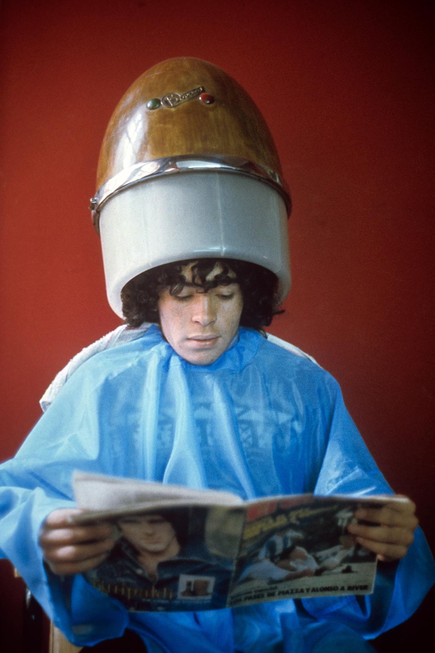 Diego Maradona sitzt beim Friseur, auf dem Kopf eine Trockenhaube