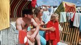 Uwe Seeler sitzt in einem Strandkorb, neben ihm seine Frau, die die Tochter abtrocknet