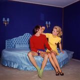 Johan Cruyff sitzt mit seiner Lebensgefährtin Danny Coster auf einem blau schimmernden Bett