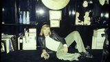 Günter Netzer liegt lässig vor einer schwarzen Schrankwand mit Büchern und Objekten
