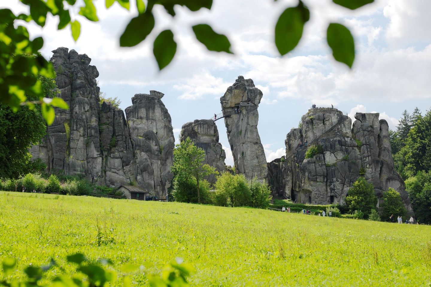 Externsteine: Sakrale Stätte aus dem 12. Jahrhundert Sandsteinfelsen mit Brücke und Mensch, davor eine Wiese