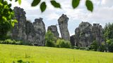 Sandsteinfelsen mit Brücke und Mensch, davor eine Wiese