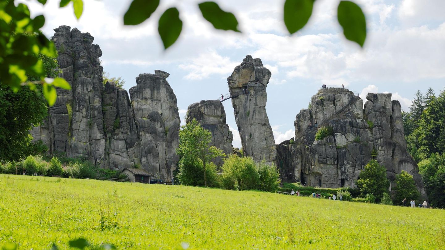 Externsteine: Sakrale Stätte aus dem 12. Jahrhundert Sandsteinfelsen mit Brücke und Mensch, davor eine Wiese