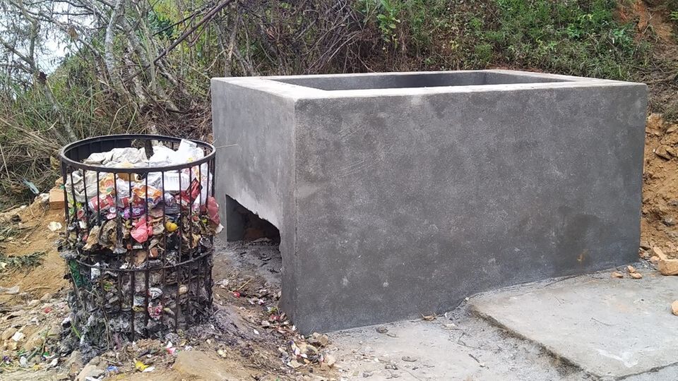 Neue Verbrennungsanlage Eine graue, frisch betonierte Verbrennungsanlage steht neben einem kleinen Drahtmülleimer