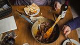 Pfanne mit Fleisch und Teller mit Brot und Glas mit Rotweinflasche auf einem Tisch