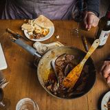 Pfanne mit Fleisch und Teller mit Brot und Glas mit Rotweinflasche auf einem Tisch