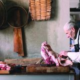 Älterer Mann mit grossem Stück Fleisch vor sich auf dem Tisch was er mit den Fingern auseinandernimmt
