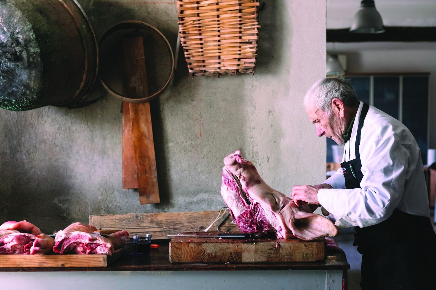Das Töten eines Schweins Älterer Mann mit grossem Stück Fleisch vor sich auf dem Tisch was er mit den Fingern auseinandernimmt