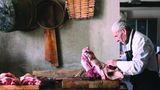 Älterer Mann mit grossem Stück Fleisch vor sich auf dem Tisch was er mit den Fingern auseinandernimmt