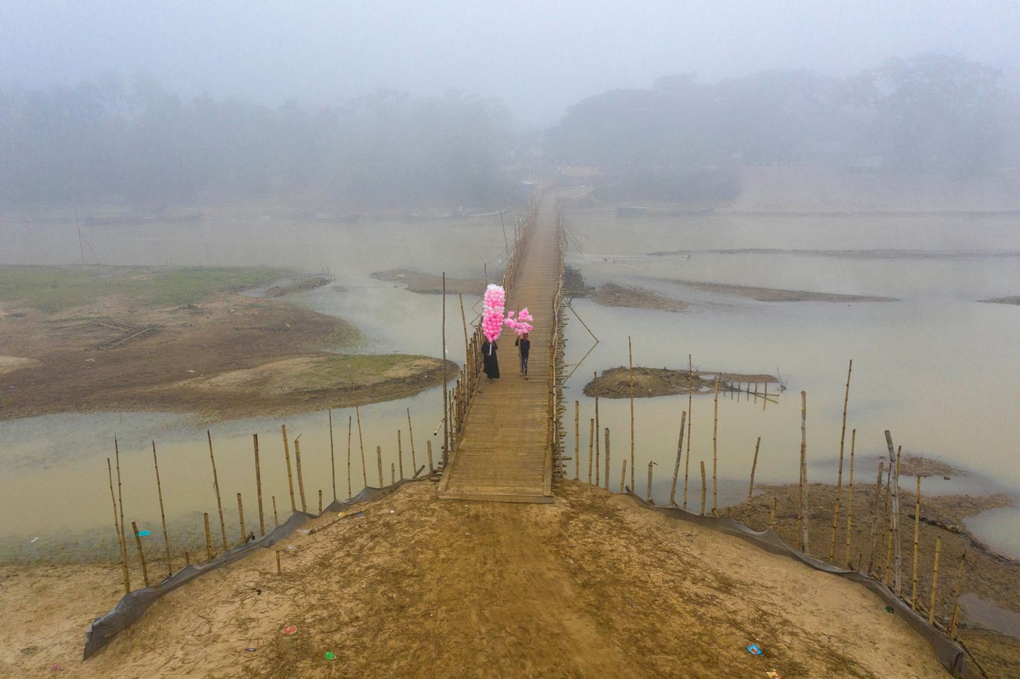 Zwei Menschen gehen über eine  Brücke und halten pinkfarbene Süssigkeiten hoch