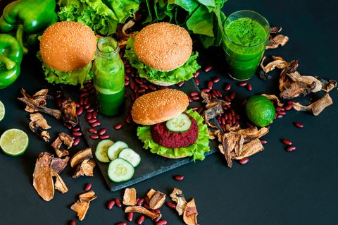 Vegane Hamburger mit Gemüse und grünem Smoothie auf schwarzem Untergrund