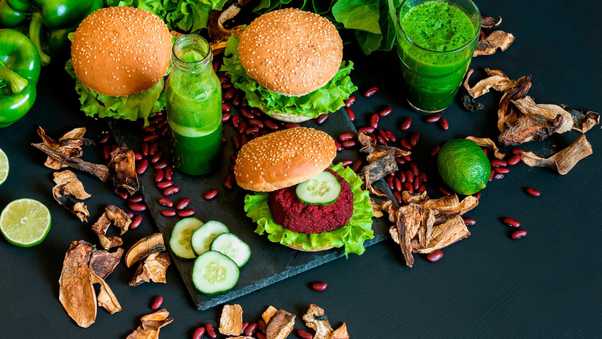 Vegane Hamburger mit Gemüse und grünem Smoothie auf schwarzem Untergrund