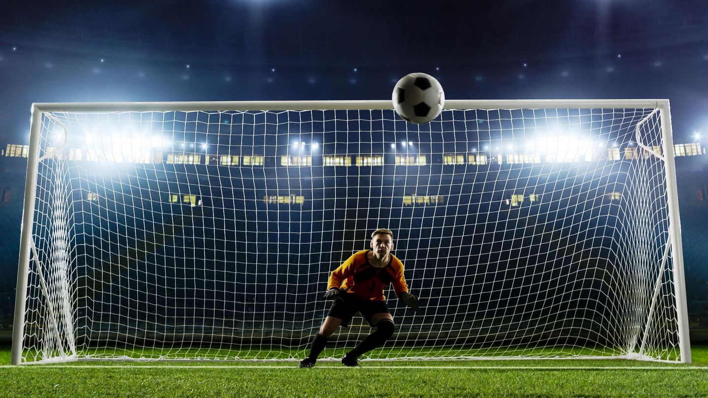 Ein Fußballtorwart blickt auf einen Ball, der auf ihn zukommt.