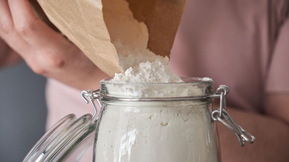 Mehlmilben bekämpfen: Jemand füllt Mehl aus einer Papiertüte in ein Bügelglas