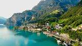 See mit Bergen und Wäldern, am Ufer liegt ein Ort, Gleise führen direkt am Ufer entlang