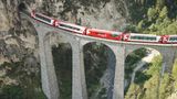 Viadukt, Felsen, Schlucht. Über die Brücke fährt ein Zug.