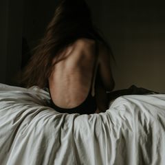 Eine dünne Frau sitzt mit dem Rücken zum Betrachter auf einem Bett