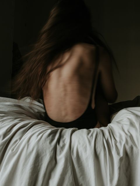 Eine dünne Frau sitzt mit dem Rücken zum Betrachter auf einem Bett