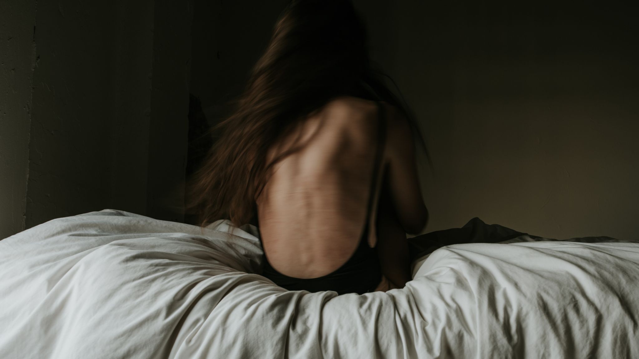 Eine dünne Frau sitzt mit dem Rücken zum Betrachter auf einem Bett