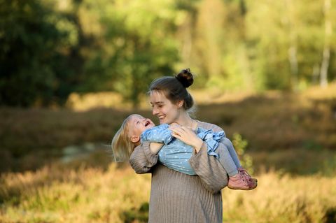 Eine junge Mutter hält ihre lachende Tochter auf dem Arm