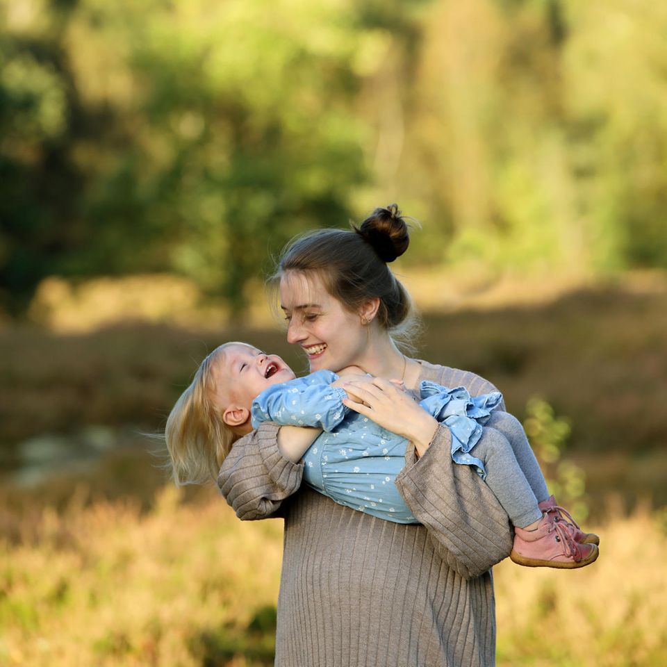 Eine junge Mutter hält ihre lachende Tochter auf dem Arm
