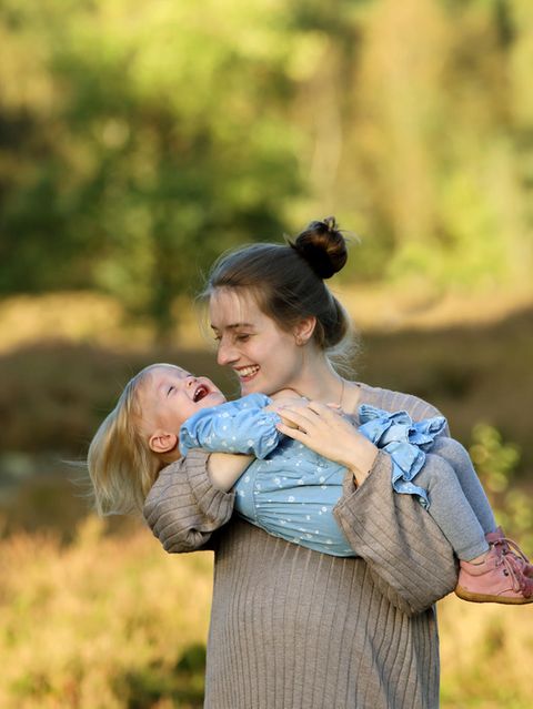 Eine junge Mutter hält ihre lachende Tochter auf dem Arm