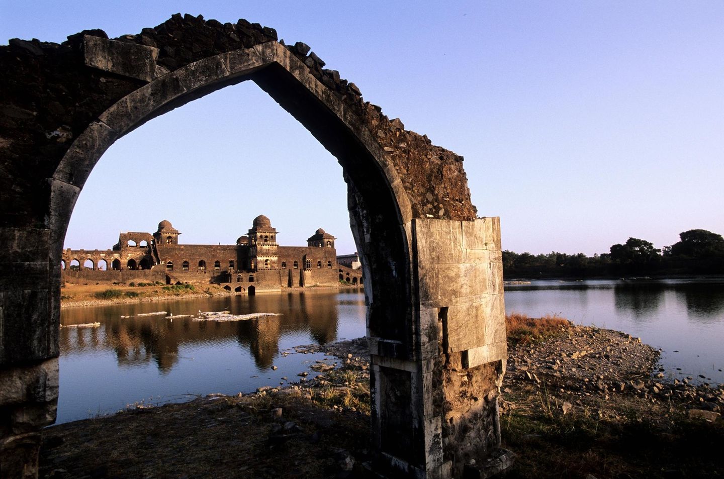 Mandu, Indien: Kultureller Reichtum in Ruinen Geisterstadt Mandu: Ein Blick durch einen gebrochenen Torbogen auf Wasser und Häuser
