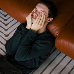 Junger Mann mit Psychose sitzt auf dem Teppich und ist an ein Ledersofa gelehnt
