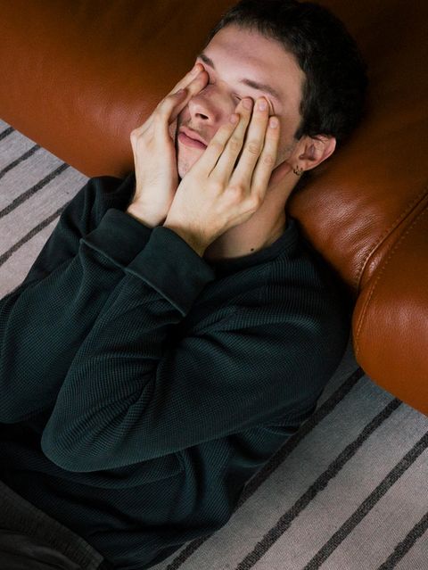 Junger Mann mit Psychose sitzt auf dem Teppich und ist an ein Ledersofa gelehnt