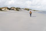 Frau geht am endlosen Strand, Dünen im Hintergrund,. Grauer Himmel.