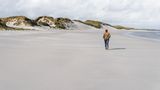 Frau geht am endlosen Strand, Dünen im Hintergrund,. Grauer Himmel.