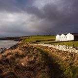 Meer, Wiese, alte Mauer: dahinter die Gebäude der Scapa Flow Destille, dramatische Wolken