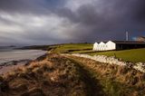 Meer, Wiese, alte Mauer: dahinter die Gebäude der Scapa Flow Destille, dramatische Wolken