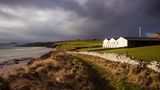 Meer, Wiese, alte Mauer: dahinter die Gebäude der Scapa Flow Destille, dramatische Wolken