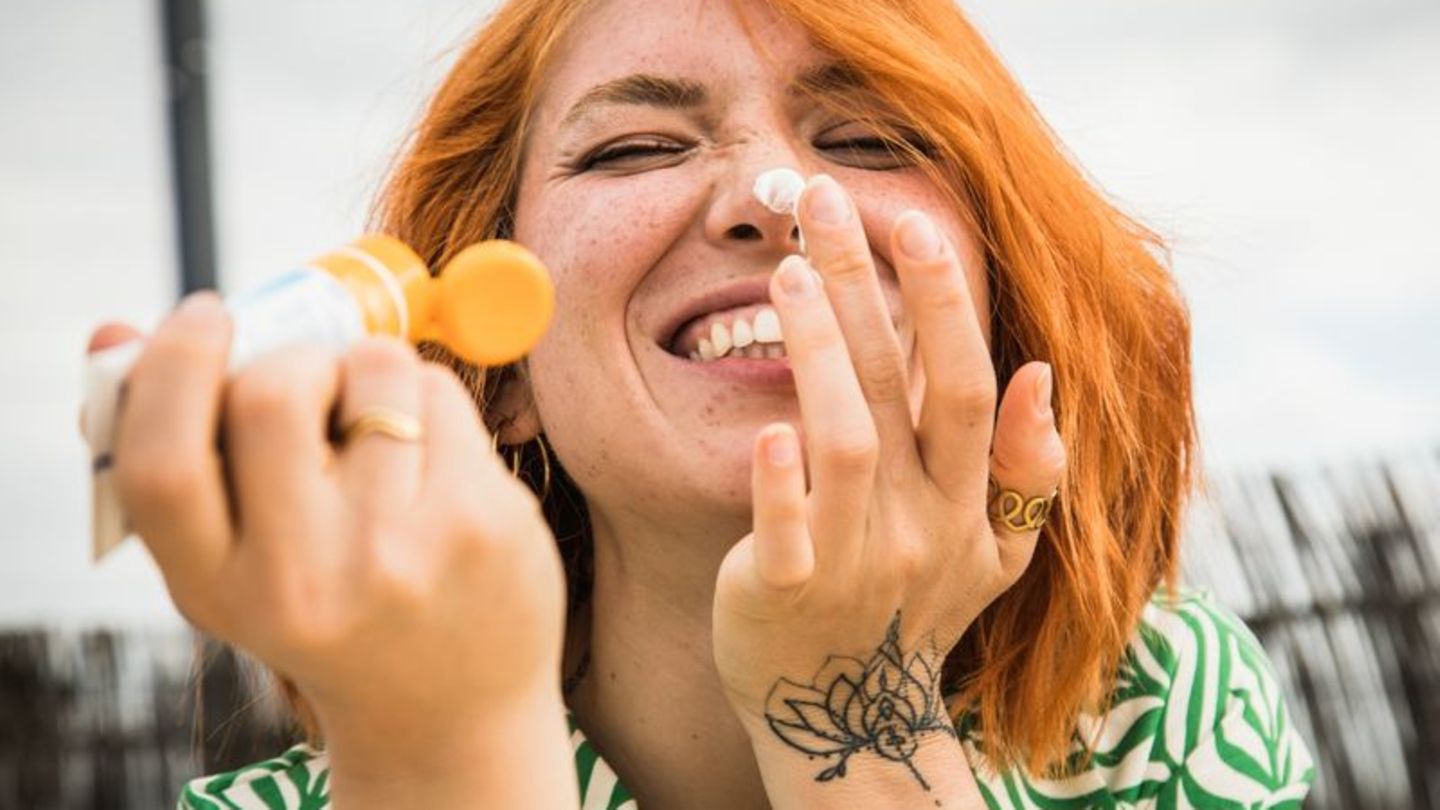 Frau cremt sich ein mit Sonnencreme und lacht dabei