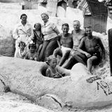 Ein Kind sitzt in einem aus Sand modellierten Rennauto, dahinter mehrere Kinder und Erwachsene
