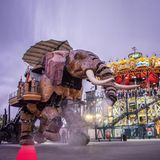 Beleuchtetes Karussell mit Meerestieren, auf dem Platz davor übergroßer künstlicher Elefant, Abendstimmung