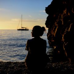 Nachdenkliche Frau sitzt im Sonnenuntergang am Meer