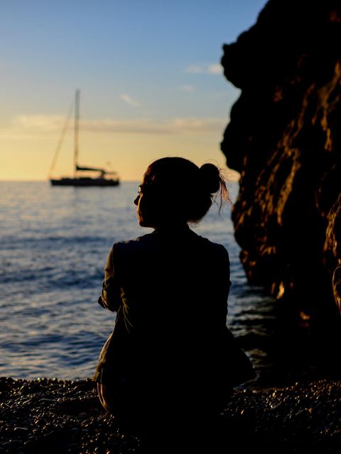 Nachdenkliche Frau sitzt im Sonnenuntergang am Meer