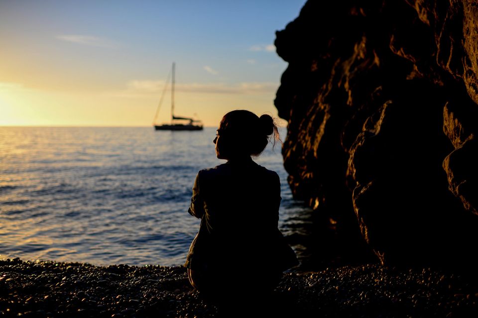 Nachdenkliche Frau sitzt im Sonnenuntergang am Meer