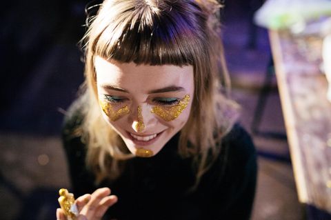 Eine junge Frau schminkt sich das Gesicht mit goldenem Glitter und lacht