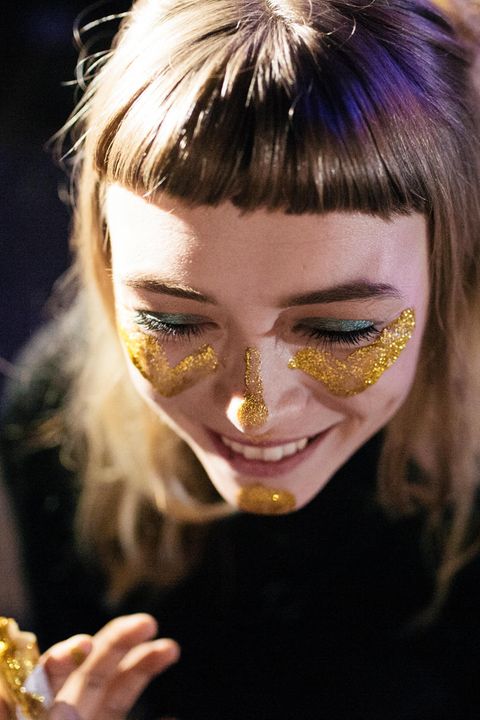 Eine junge Frau schminkt sich das Gesicht mit goldenem Glitter und lacht