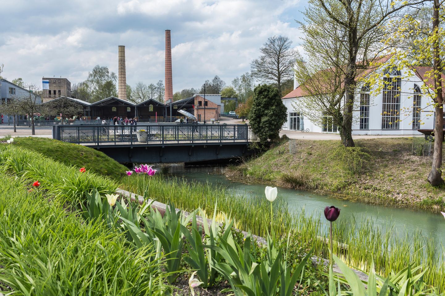 Auf einem ehemaligen Industriegelände: Familiengarten Eberswalde Schornstein, alte Gebäude, davor ein blühender Garten am Kanal