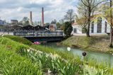 Schornstein, alte Gebäude, davor ein blühender Garten am Kanal