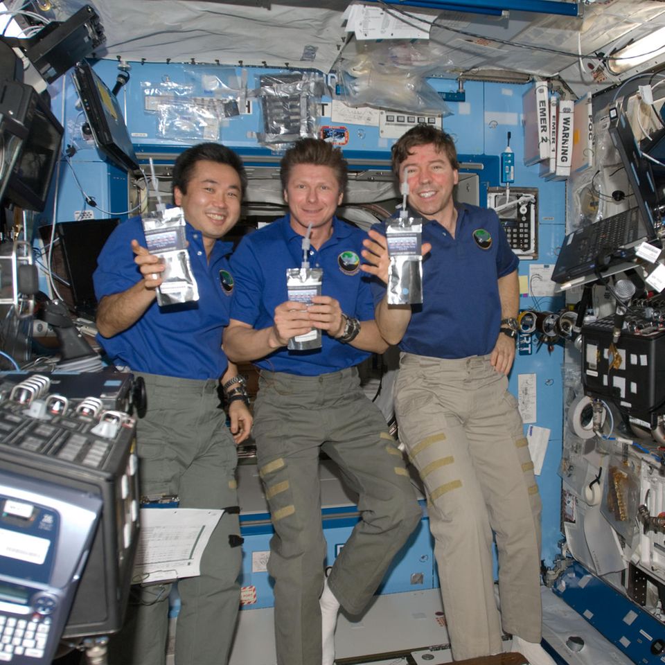 Drei Astronauten auf der ISS halten Trinkpäckchen hoch
