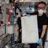 Mann steht mit Maske in technischer Anlage und hält großen weißen Beutel hoch