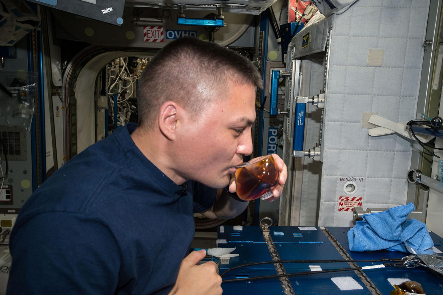 Die Kraft der Kapillaren Astronaut trinkt Kaffee aus einer seltsam geformten Tasse