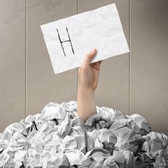 Eine Hand ragt aus einem Berg zerknüllter Zettel